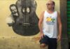 Brazilian guitarist Phill Fest Sings a Slice of Life, standing in front of a yelllow wall featurng a street art guitar.