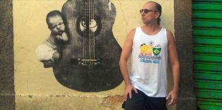 Brazilian guitarist Phill Fest Sings a Slice of Life, standing in front of a yelllow wall featurng a street art guitar.